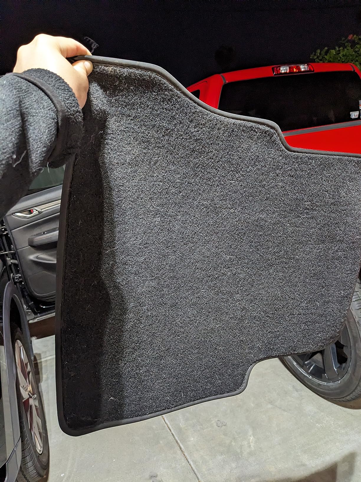 A hand holding up a black car floor mat with a raised edge, showing the underside with no visible dirt or debris.