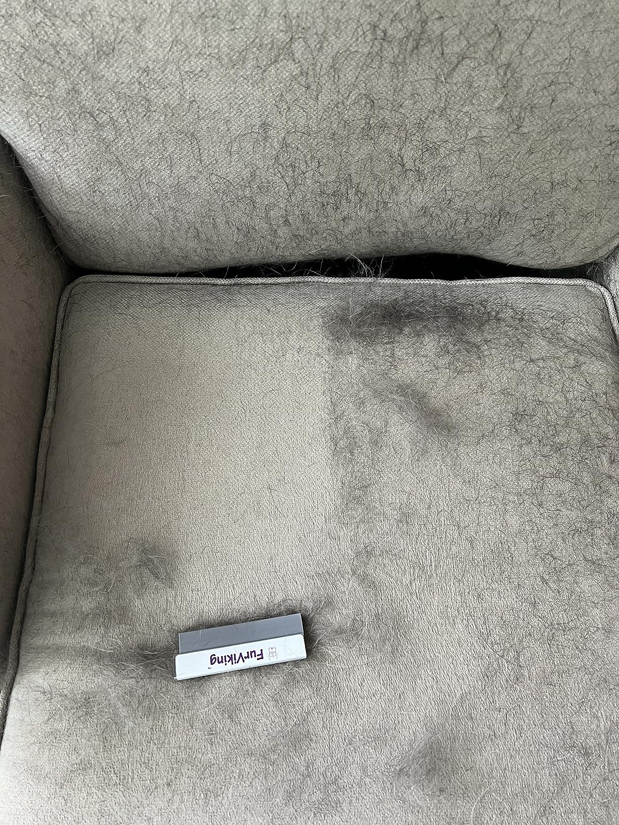 Close-up of a gray sofa cushion with a noticeable difference between the left side, covered in pet hair, and the right side, where the FurViking pet hair remover tool has been used to remove the hair.